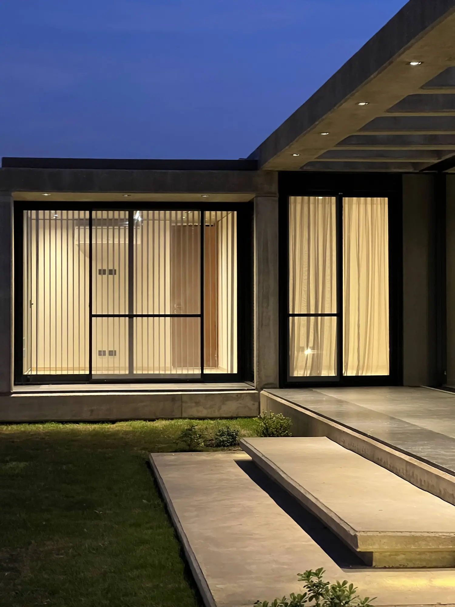 Ventanales iluminados y escalones de hormigón al anochecer, en una vivienda de Invernón Arquitectos