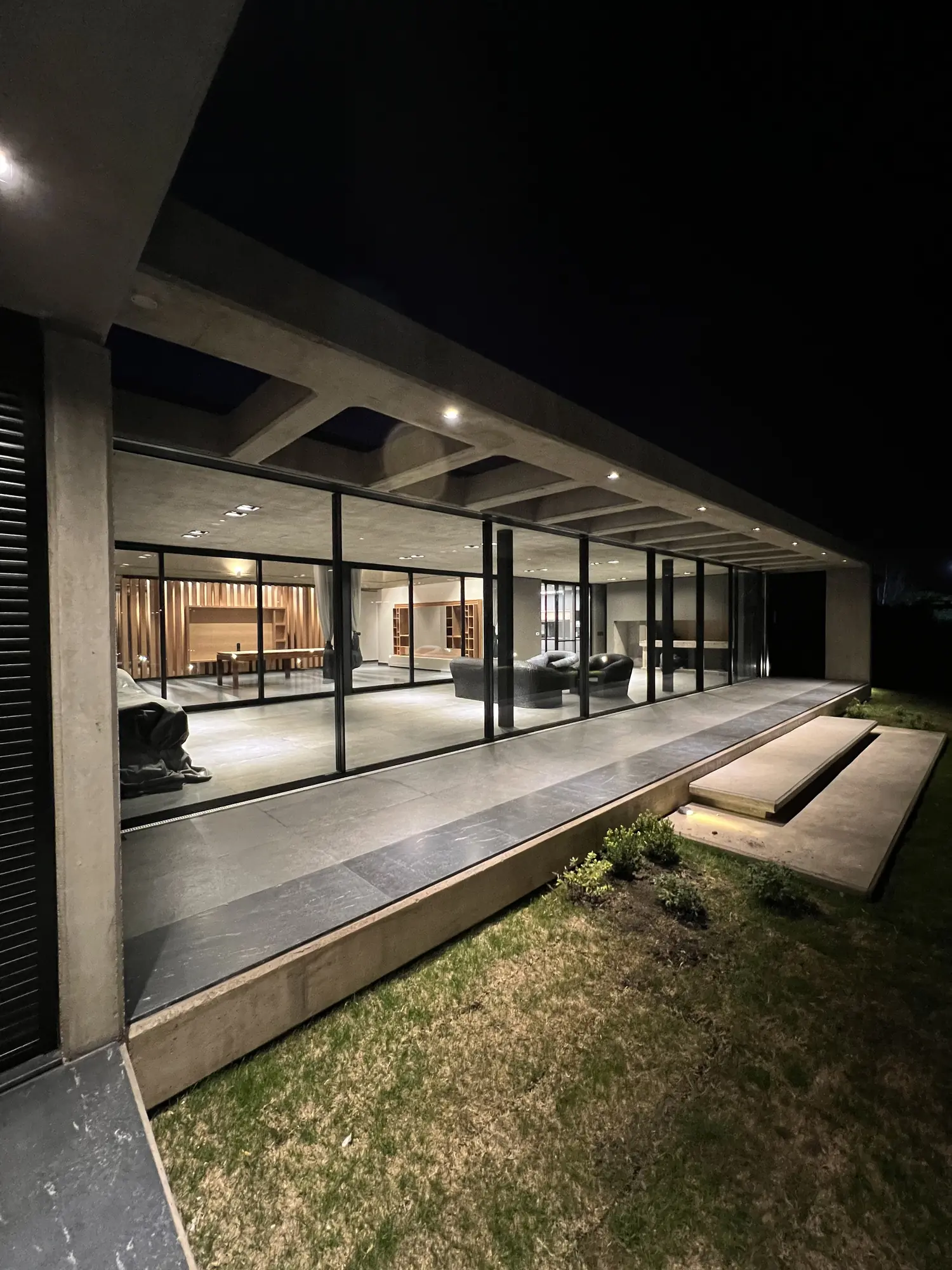 Galería vidriada de noche, con escalones de hormigón sobre el jardín